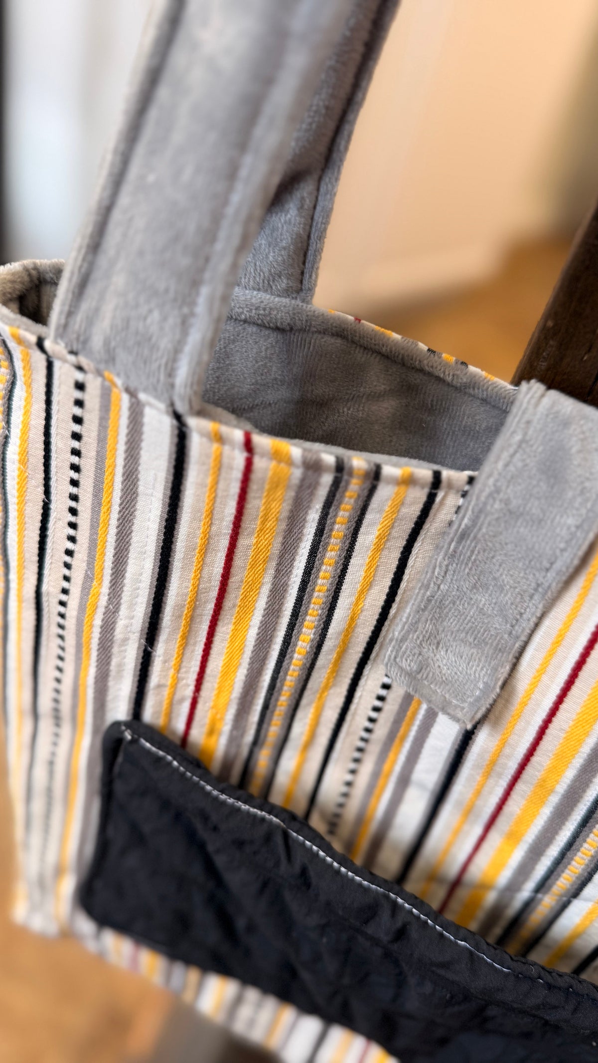 Close-up of a striped fabric tote bag with gray handles and a black front pocket, hanging indoors.