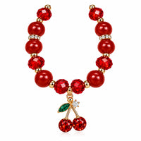 A red beaded necklace featuring faceted red beads, gold-toned spacer rings with clear rhinestones, and a cherry charm at the center with a green leaf and red crystal cherries.