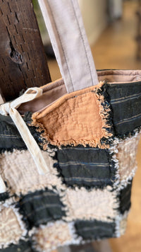 A close-up of a handmade patchwork tote bag made from flannel and beige linen fabrics